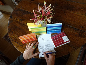 woman's hands writing in an open notecard with a stack of striped notecards in the background
