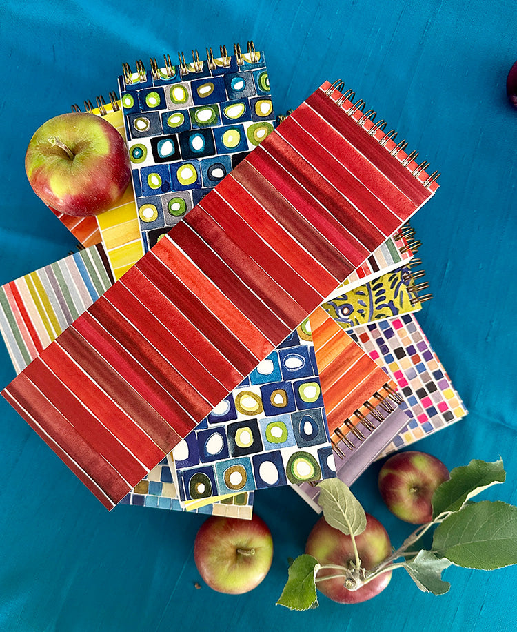 colorful stack of narrow notebooks used for list-making and some apples