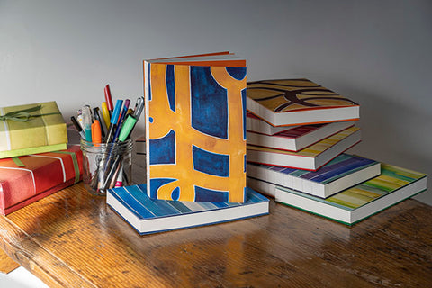 desktop full of colorful journals stacked with one blue and gold graphic journal standing up 