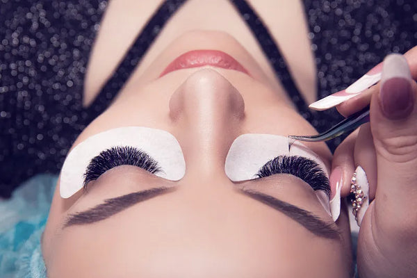 Una mujer recibe extensiones de pestañas voluminosas en un salón de belleza.