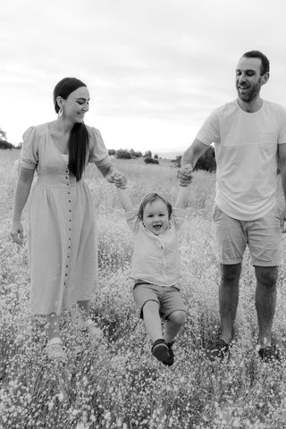 Tom Briscoe (maker and owner) on the right with his partner Hannah on the left, both swinging their son Alfie (in the middle). Black and white image. Standing in a Tasmanian field of wild flowers. Family with a little boy smiling.