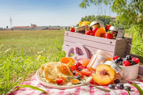 Various fruits such as peaches, strawberries, and blueberries arranged on a red and white checked picnic blanket laid out on grass.