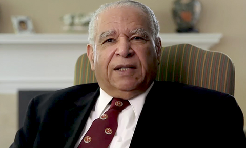 Albert B. Crum seated in a chair wearing a suit and tie