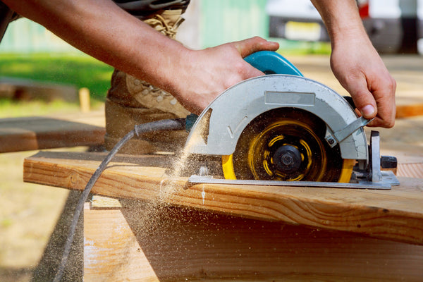 Close-up image of a person using a hand-held circular saw to make an angled cut on a 2x6 board.