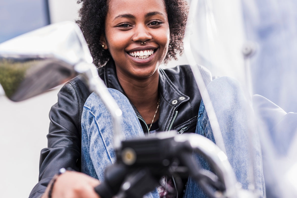 Smiling young woman after purchasing used motorcycle with Luimoto seat cover for additional value