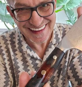 A person smiling while holding a knife, wearing glasses and a patterned shirt.