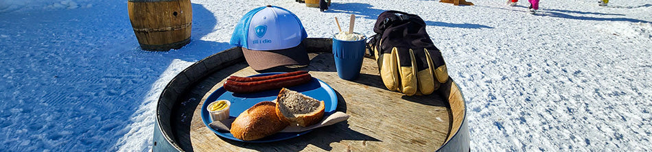 Till I die hat sitting on a wine barrel with ski gloves and sausages.