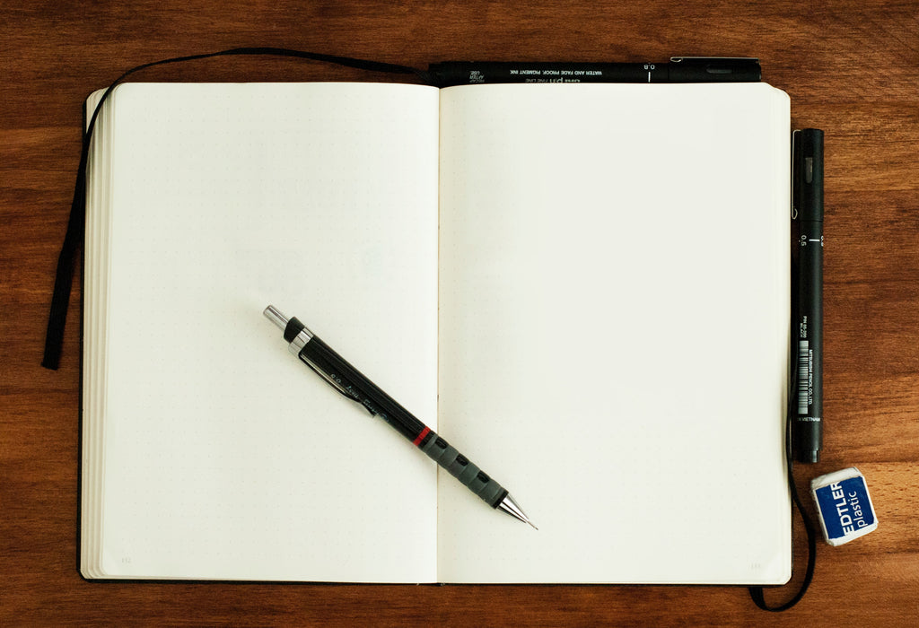 Cuaderno en blanco sobre mesa de madera con portaminas y goma de borrar. 