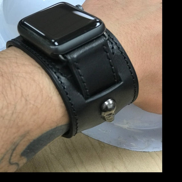 A wrist shot of an Apple Watch featuring a black leather band with a sterling silver skull stud. The watch face displays the time in digital format and includes various health and fitness tracking features. The black leather band adds a stylish touch to the device, while the sterling silver skull stud creates an edgy and unique look.