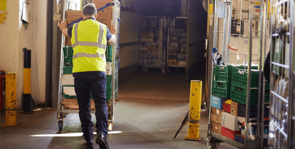 An employee in a yellow high vis pushing a quiet mark certified roll cage.