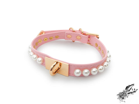 pink and gold choker made of vegan leather, with a gold hardware plate with U shaped stud in the centre and white pearl studs around either side