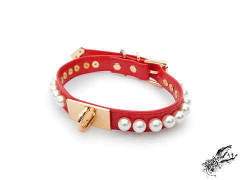 red and gold choker made of vegan leather, with a gold hardware plate with U shaped stud in the centre and white pearl studs around either side