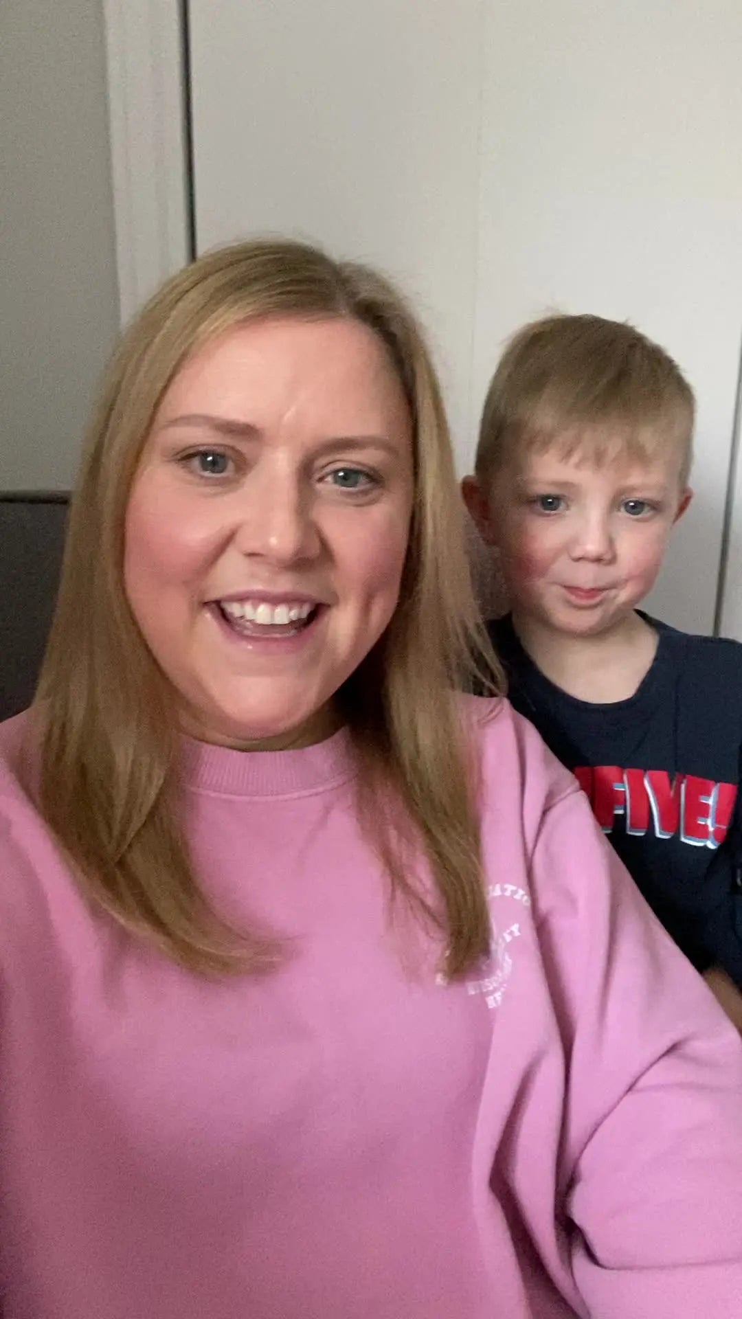 A woman and a child smile at the camera indoors.
