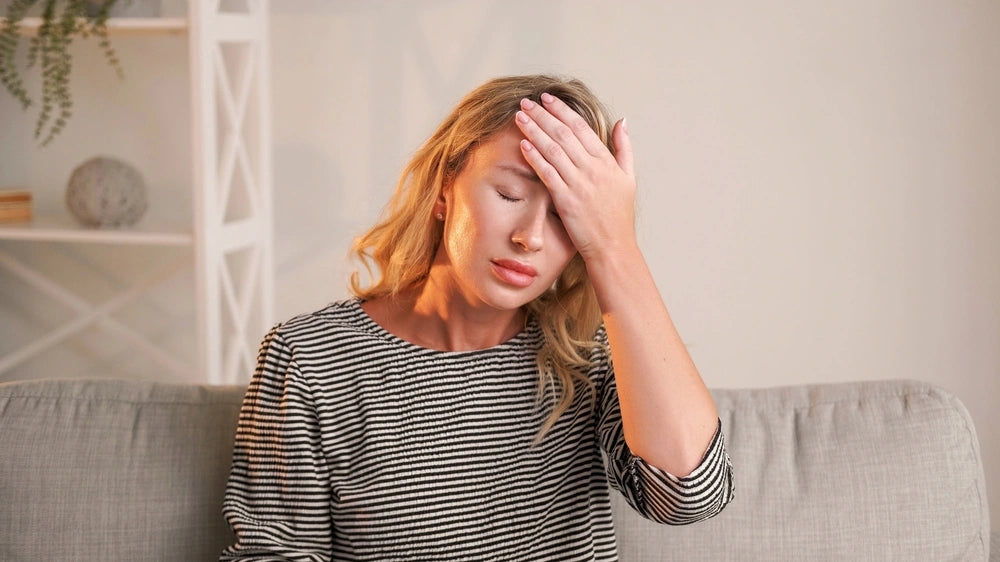Fatigued woman holding her forehead at home representing low energy and stress symptoms linked to NAD+ depletion