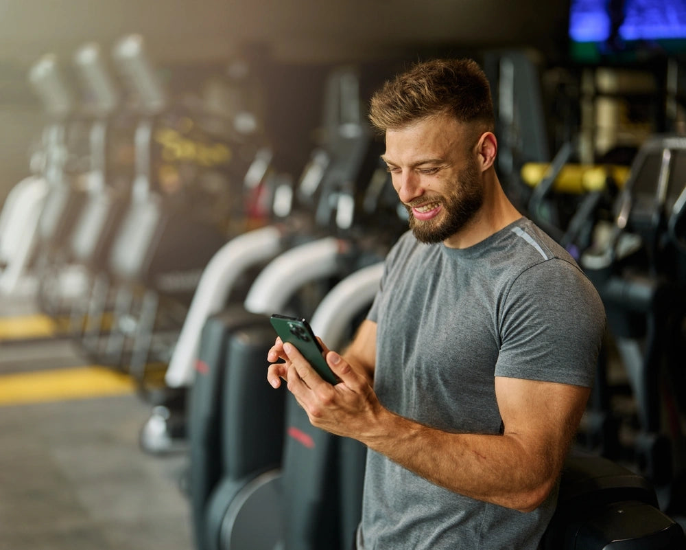 Healthy young man checking phone after gym workout symbolizing increased energy and fitness benefits associated with sermorelin therapy