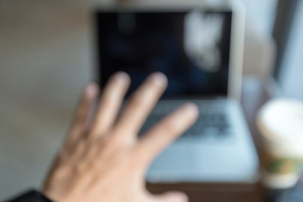 Person experiencing blurred vision while reaching for a laptop with a cup of coffee nearby, symbolizing the potential side effect of vision problems like blurred or dim vision during Vuity™ treatment