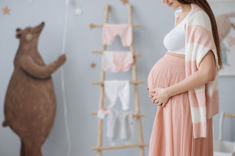 Une femme enceinte, tenant son ventre et face aux vêtements de son bébé, pr^te pour la maternité