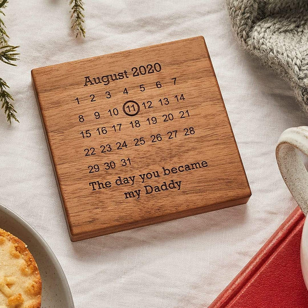 A wooden coaster engraved with a calendar design; underneath the calendar reads "The day you became my Daddy"