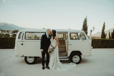 A wedding photo of bride and groom stood in front of a campervan