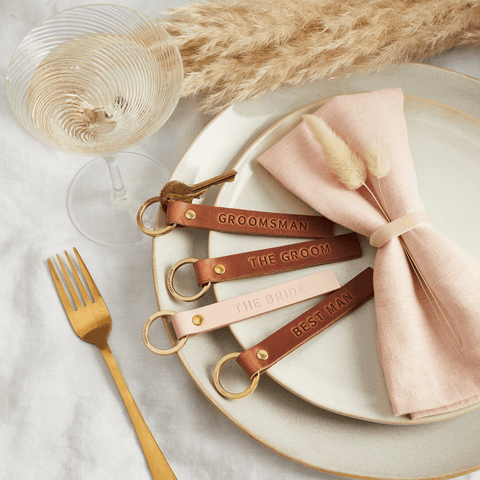 A wedding dinner table with personalised leather keyrings scatter on top as place settings - the brown and pink leather keyrings are personalised for the bride, groom and wedding party