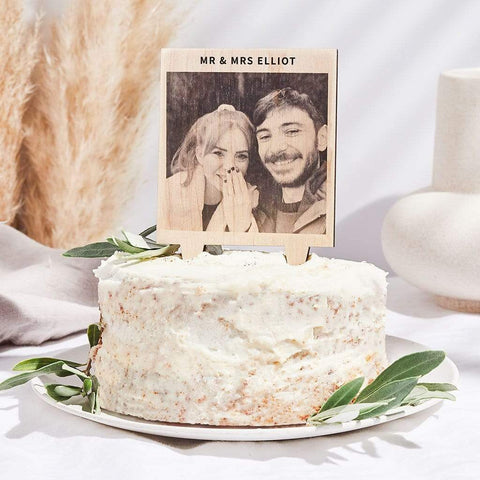 A rustic wedding cake with a personalised wooden wedding cake topper on the top, showing a photograph of a newly engaged couple and the text 'Mr & Mrs Elliot'