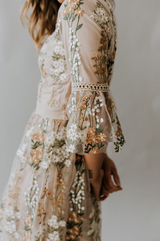 Fair skinned person's profile wearing a cream floral embroidered tulle dress with ruffle sleeves