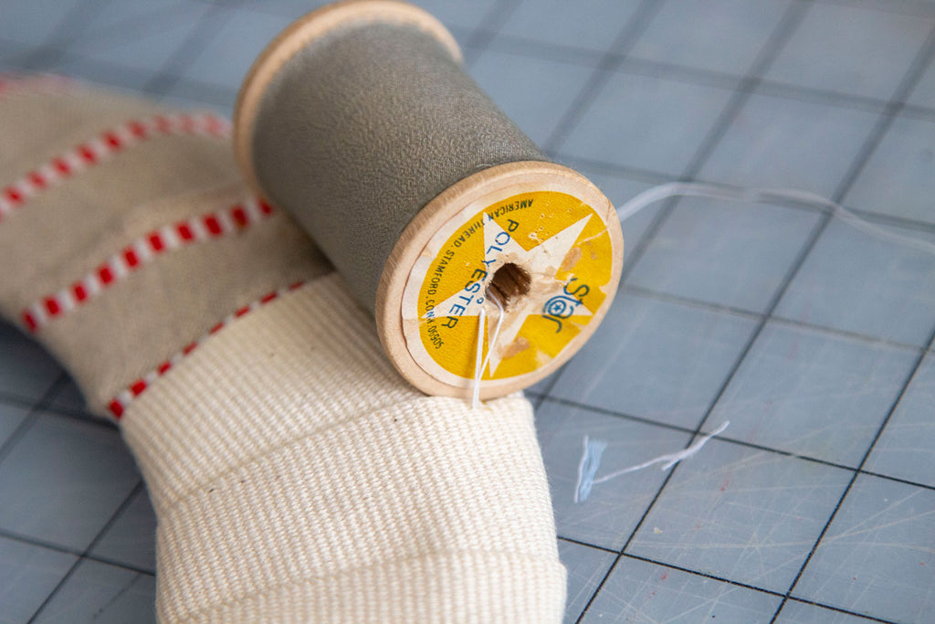 The grey spool has been secured with 2-3 stitches through its center onto the wreath frames wrapping