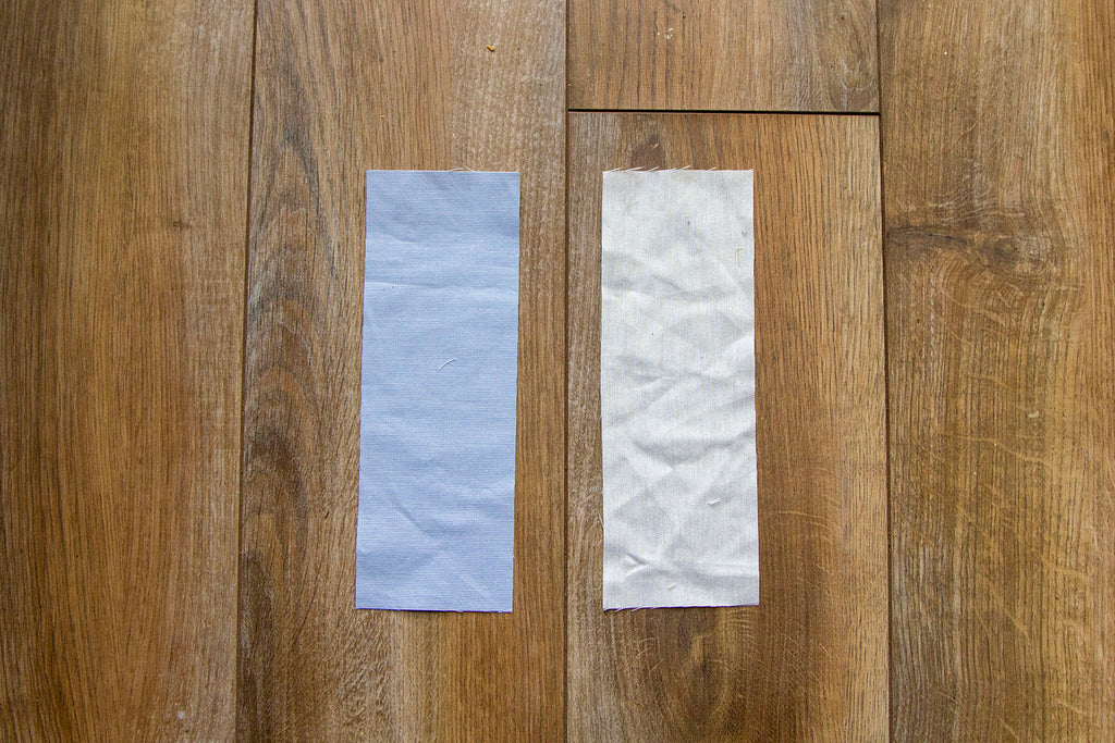 A blue fabric rectangle sits to the left of a muslin fabric rectangle on top of a dark wooden floor