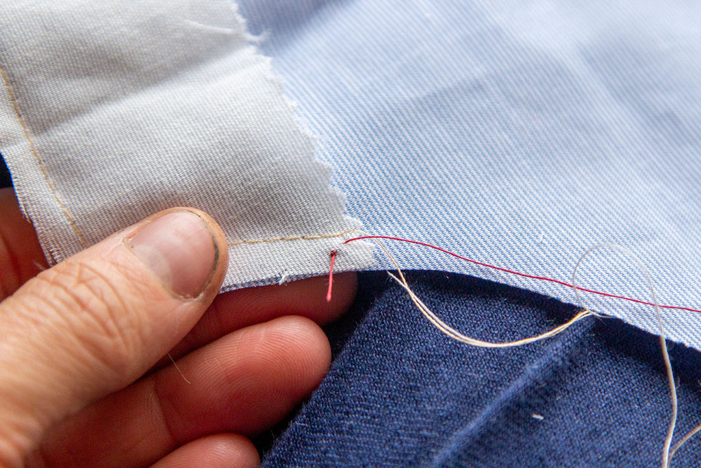 The single red thread has been pulled through the wrong side of the blue garment and basted muslin interfacing. It is between the edge of the fabric and the basting stitches. 