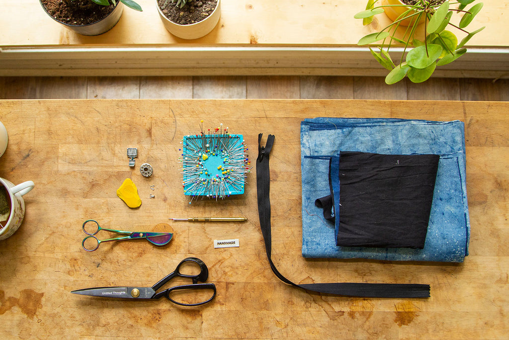 A flat lay of the supplies needed for this sewing project including scissors, hook and eye, zipper, pins, etc. 