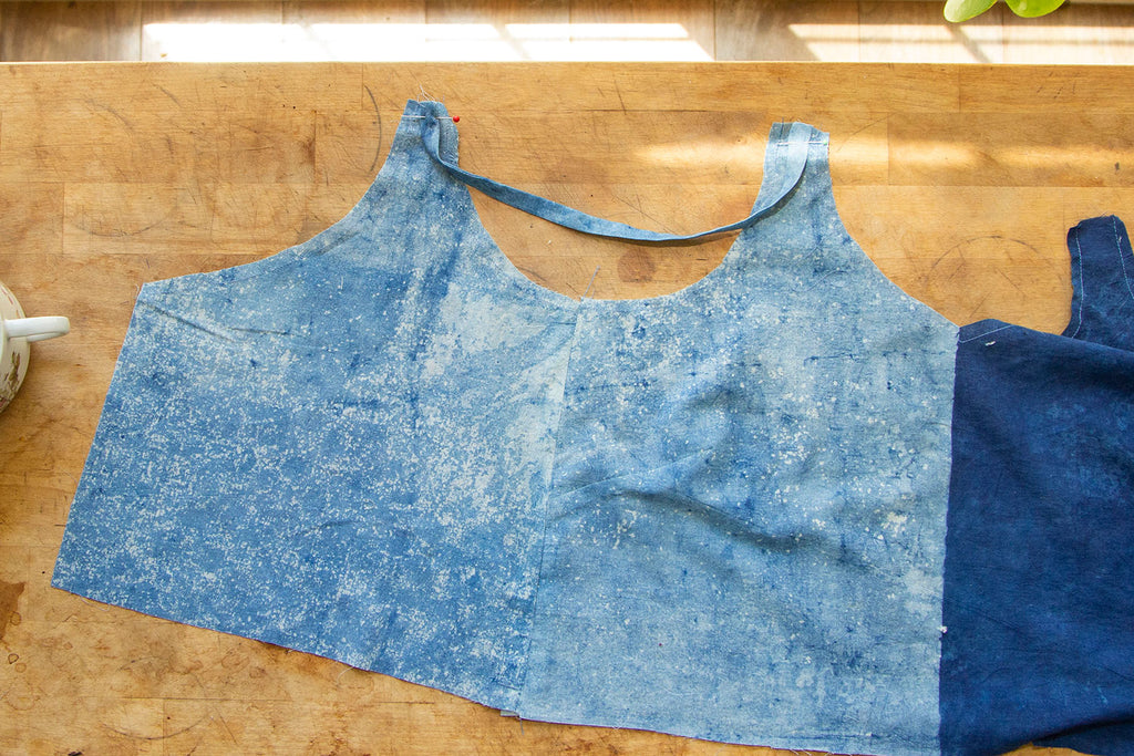 A dual toned blue bodice is laid out on a wooden cutting table with a strap basted to it's strap openings. 
