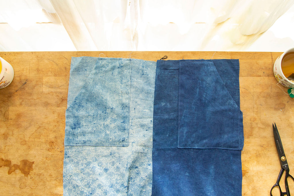 A dual toned blue pair of pants with patch pockets is laid out on a natural cutting board with light streaming from a window