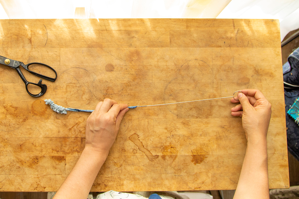 A pair of white hands is pulling the waist tie right side out using a rouleau turner. Underneath this action is a wooden chopping block