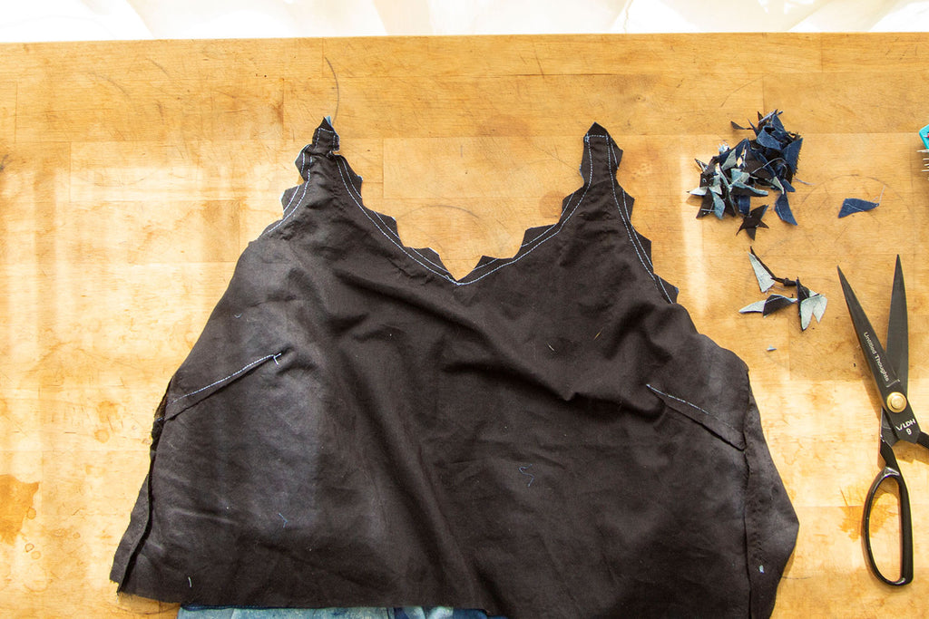 A flat lay of the black lining with loads of little triangles cut out from the front neckline. The scraps of the fabric cut out are sitting in the upper right corner with a pair of black scissors just below them 