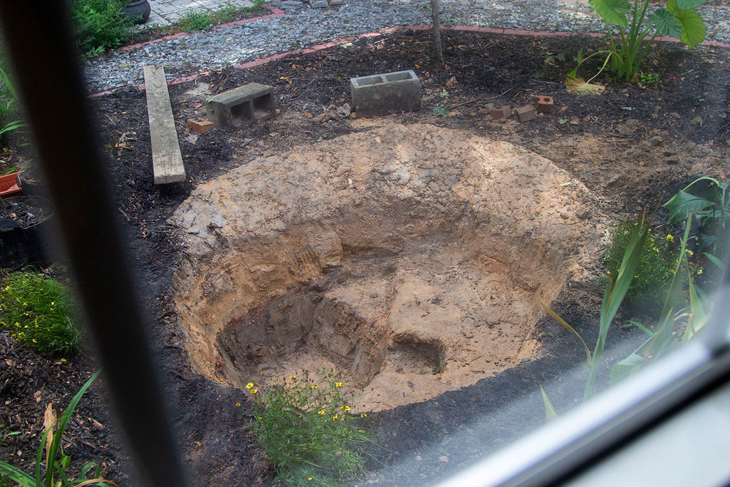 The fully dug pond complete with a gentle slope on one side of the pond followed by a shelf roughly a foot down then a second shelf 2 feet down as well as a small "cave" that will become a full cave once a rock has been laced over top of it.