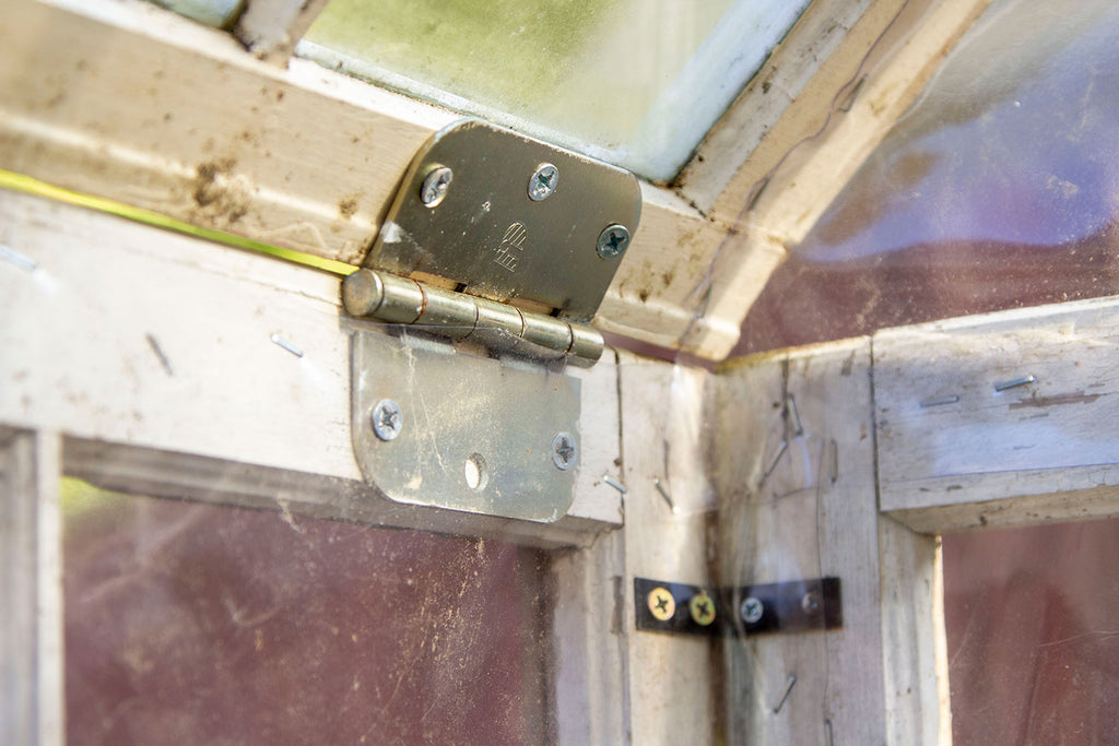 Close up of gold hinges on the inside of the greenhouse attaching the roof to the walls a an obtuse angle. 