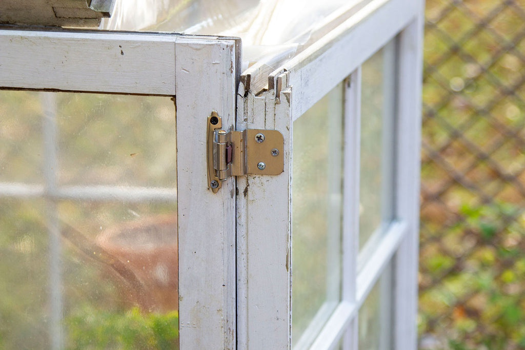 Close up of a silver hinge attached to the outer door of the greenhouse