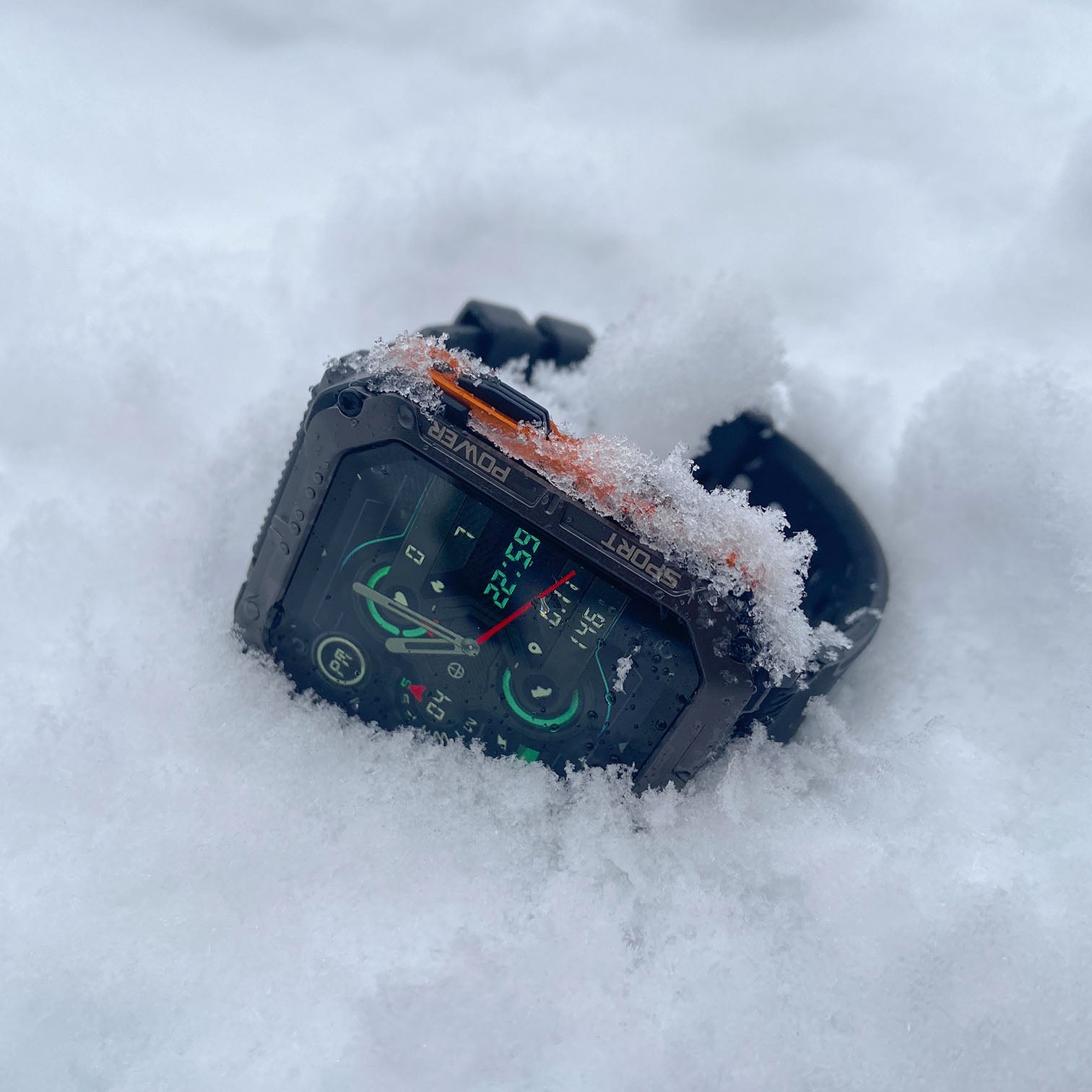 Digital smartwatch partially buried in the snow.