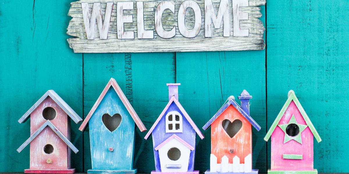 a welcome sign hung above a row of colorful birdhouses