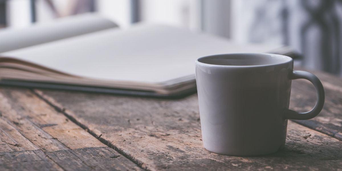 a wooden table with a white mug on it and a journal open to blank pages