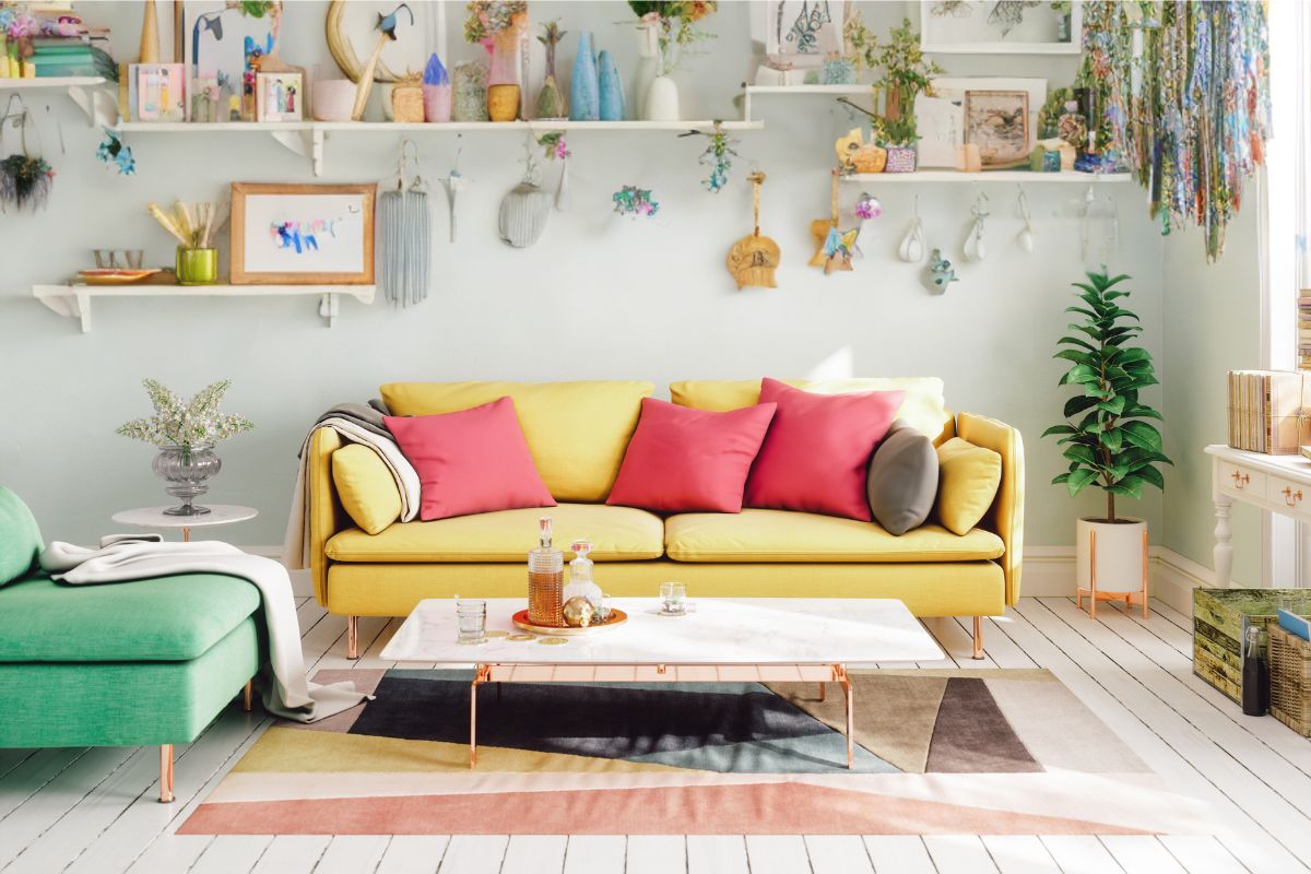 a whimsical living room with a yellow couch, pink pillows, and boho decor on the wall