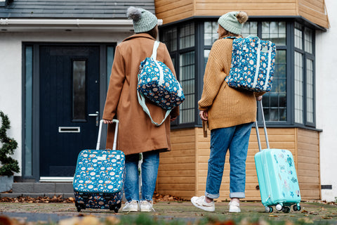 image shows two people entering a house with the little luggage co kids suitcase, tote bag and backpack