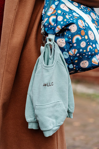 image shows a jumper embroidered with #LLC hanging from a coat loop on the little luggage co tote bag