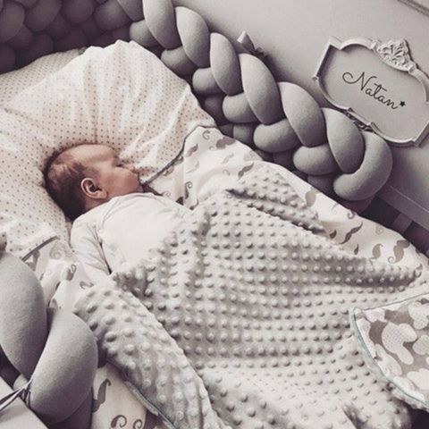 Un enfant endormi dans son lit avec une tresse de lit bébé grise autour de lui
