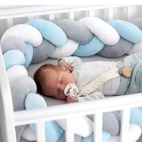 Un enfant endormi dans son lit avec une tresse de lit bébé bleue autour de lui