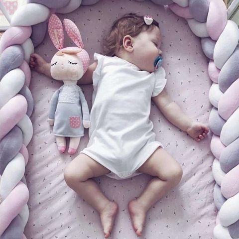 Une petite fille dormant dans son lit avec une tresse de lit bébé blanc-gris-rose autour d'elle