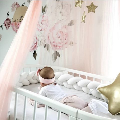 Un enfant allongé sur le ventre dans son berceau avec une tresse de lit bébé blanc autour de lui