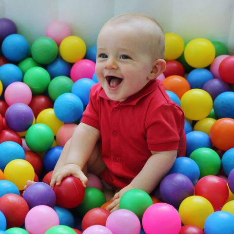 Bébé joyeux en chemise rouge assis parmi des balles à piscine multicolores.