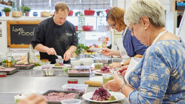 Older and younger women wearing aprons cooking with the chef at the cookery school