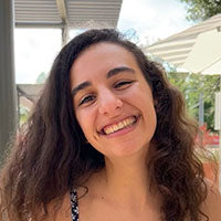 Woman with long curly hair smiling brightly outdoors.